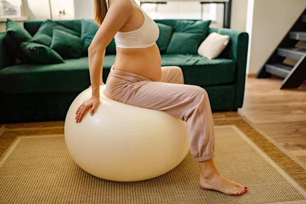 Těhotná žena cvičí doma v obývacím pokoji v sedě na sedacím míči.